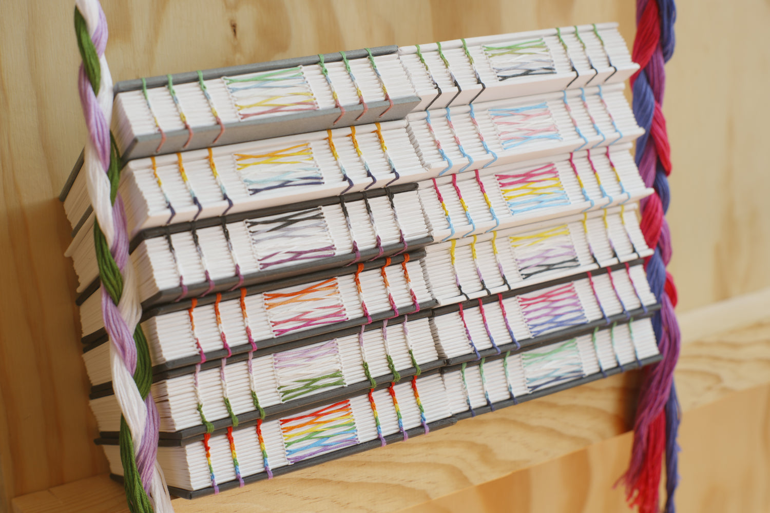 Two stacks of handmade Pride themed journals with exposed stitching in various Pride flag colors.